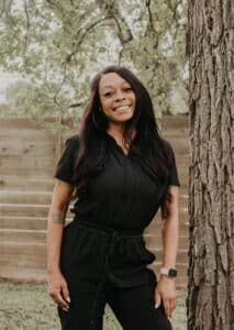 Smiling woman in black outfit outdoors near a tree at Heartwood Recovery.