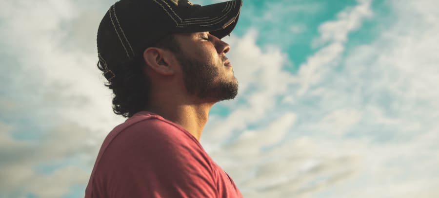 Man practicing mindful breathing, with a serene sky as the backdrop, symbolizing tranquility and the journey of mindfulness and addiction recovery.