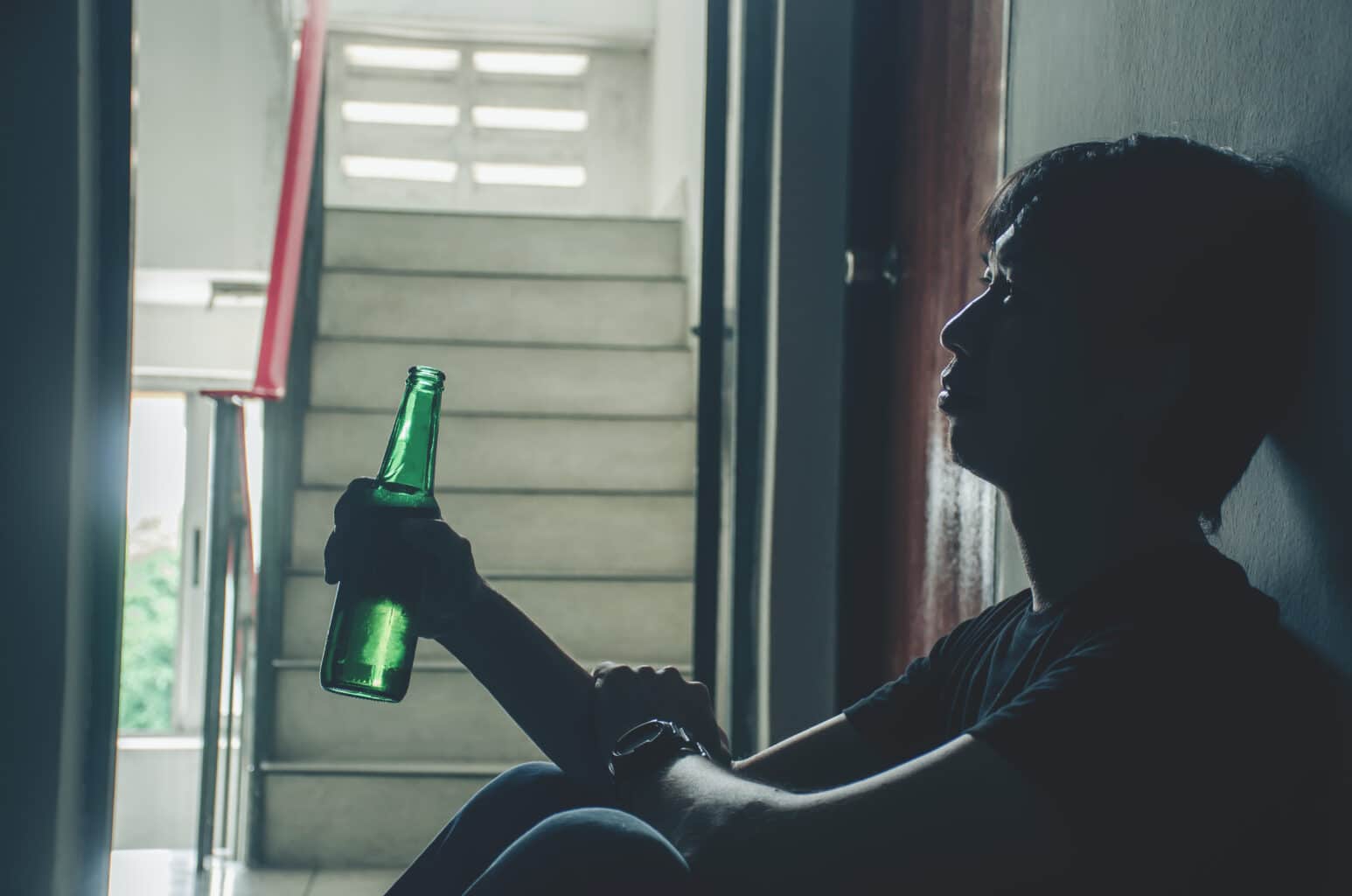 Man sitting alone on steps holding a beer bottle as the early buzz wears off.