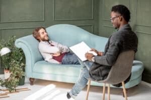 A man smiling while laying on a couch and speaking with a therapist for the topic how much does iop cost with insurance​.