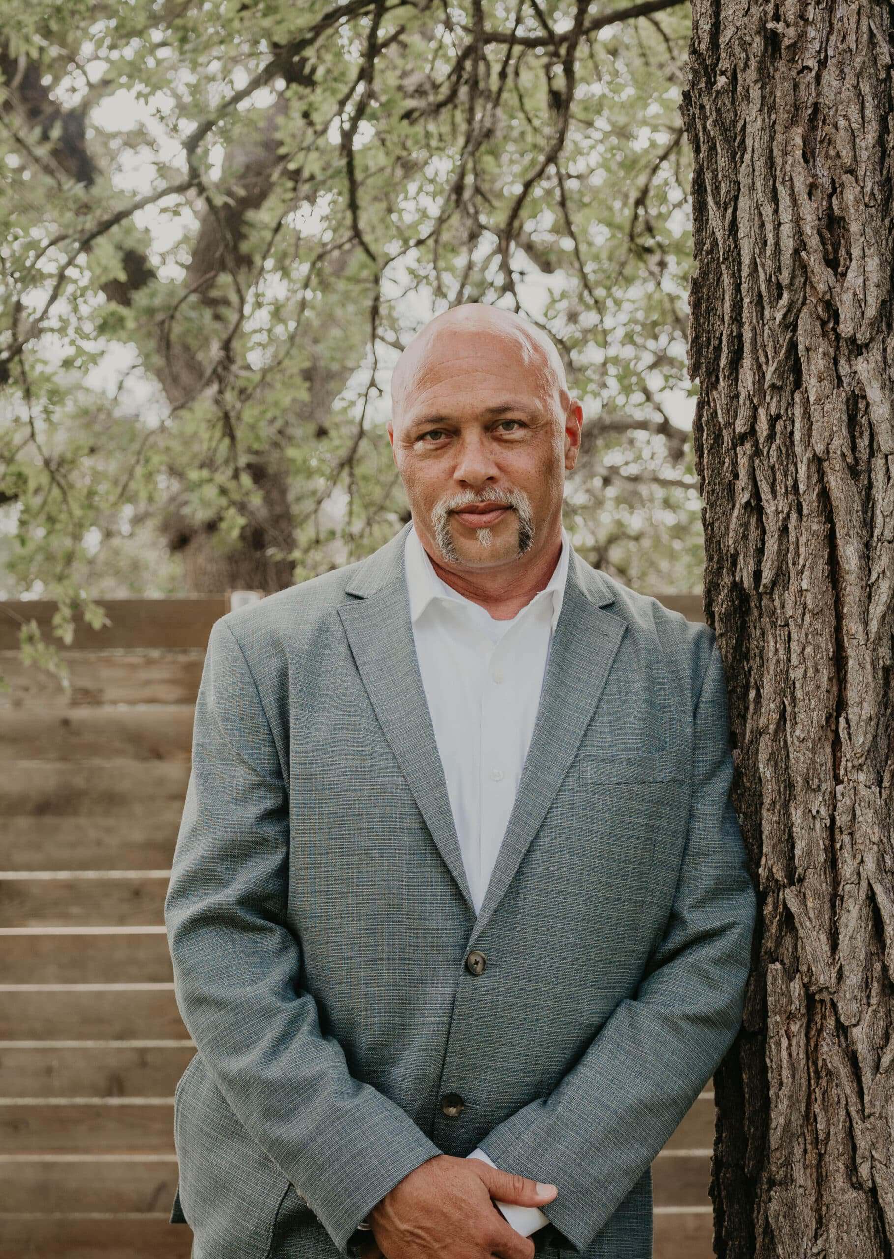 Professional man in a gray suit standing outdoors near a tree.