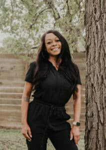 Smiling woman in black outfit outdoors near a tree at Heartwood Recovery.